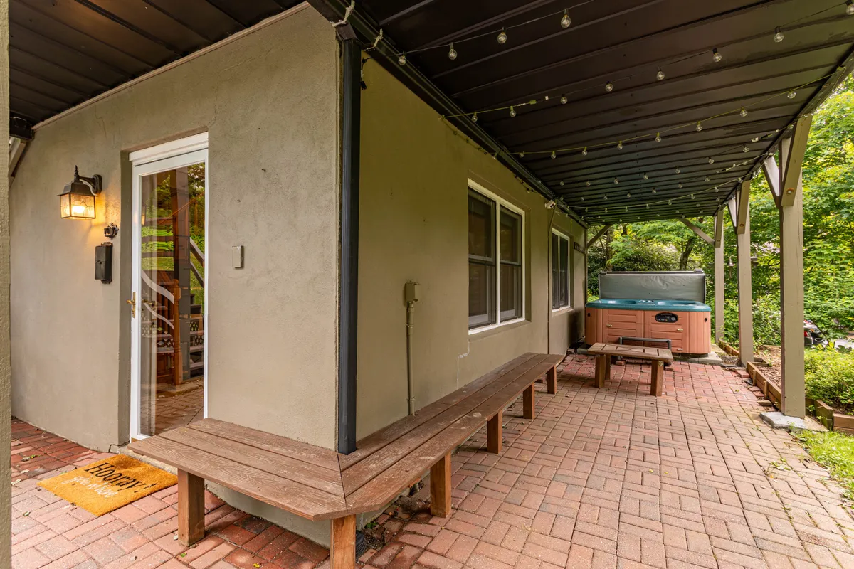 This image shows a covered porch featuring a bubbling hot tub, wooden benches, and a welcoming outdoor atmosphere. String lights add warmth, while the natural wood construction and open-air environment invite guests to enjoy relaxation surrounded by fresh mountain air.