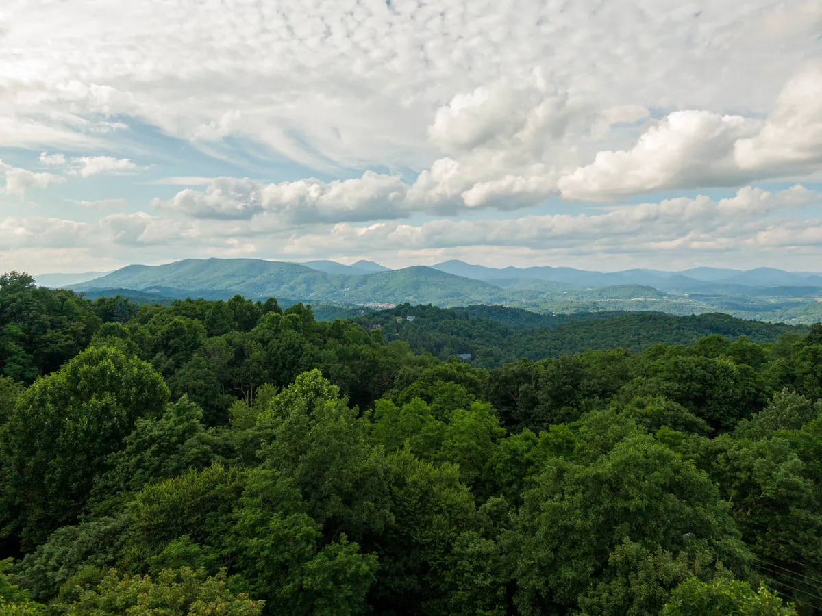 A sweeping view of a mountain range set against dense greenery and a cloudy sky, evoking a sense of adventure and natural beauty. The scene suggests the proximity of hiking and outdoor exploration opportunities.