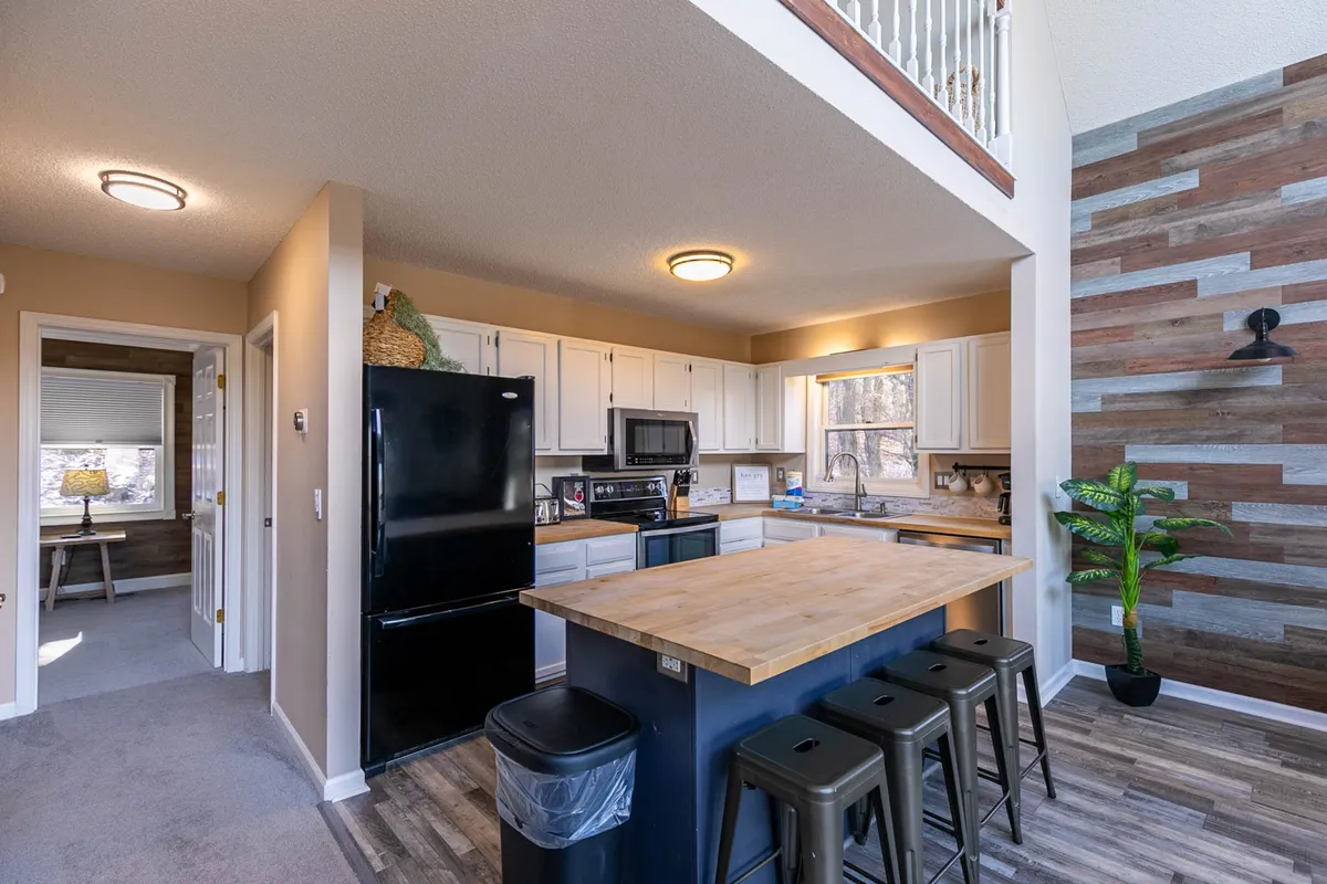 A close-up view of the modern kitchen with a central island, black appliances, a wood accent wall, and a touch of greenery from a potted plant. The setting is ideal for cooking, sharing stories over breakfast, or preparing snacks for a group.