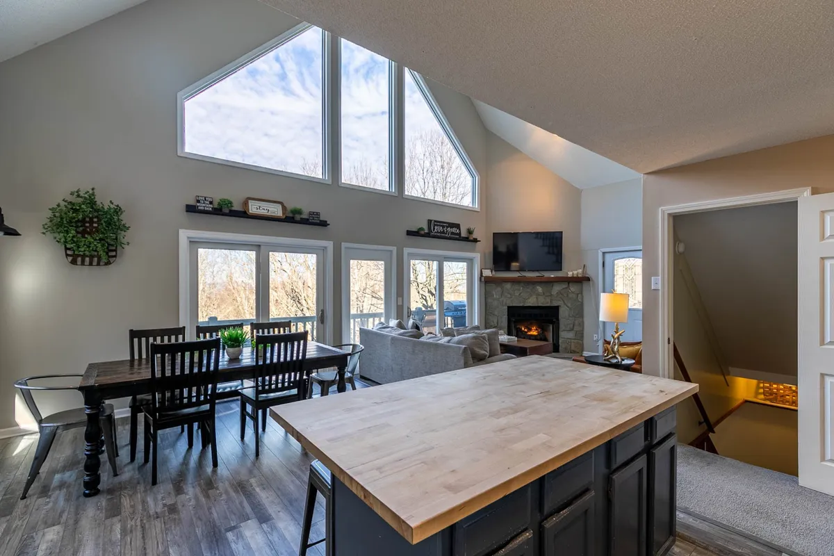 A warm, inviting space with large windows letting in natural light and scenic views, a kitchen island, a dining table set for meals, and a cozy fireplace. The area feels perfect for both intimate dinners and relaxed family gatherings, tying in mountain ambiance and comfort.