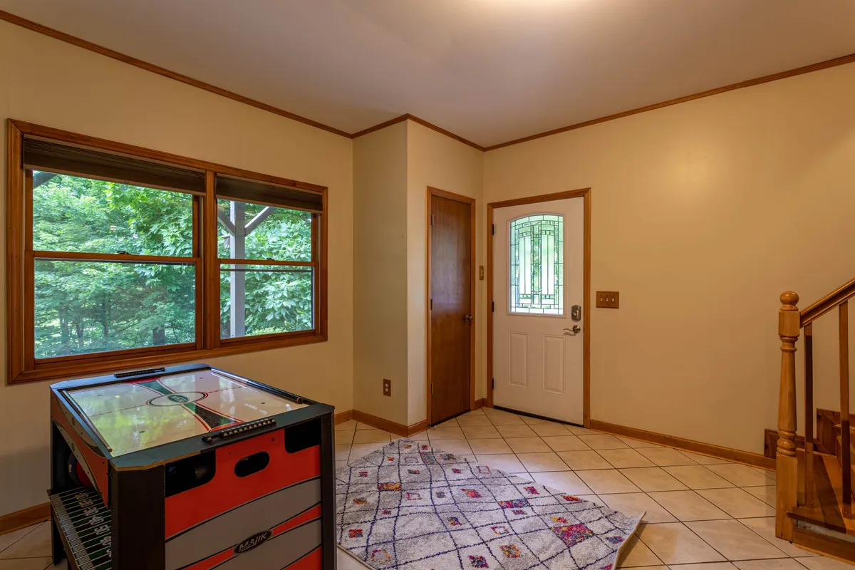 A playful and inviting area with an air hockey table, windows allowing natural light, the home’s front door, and a staircase leading to other parts of the house. The setup encourages group play and casual fun.