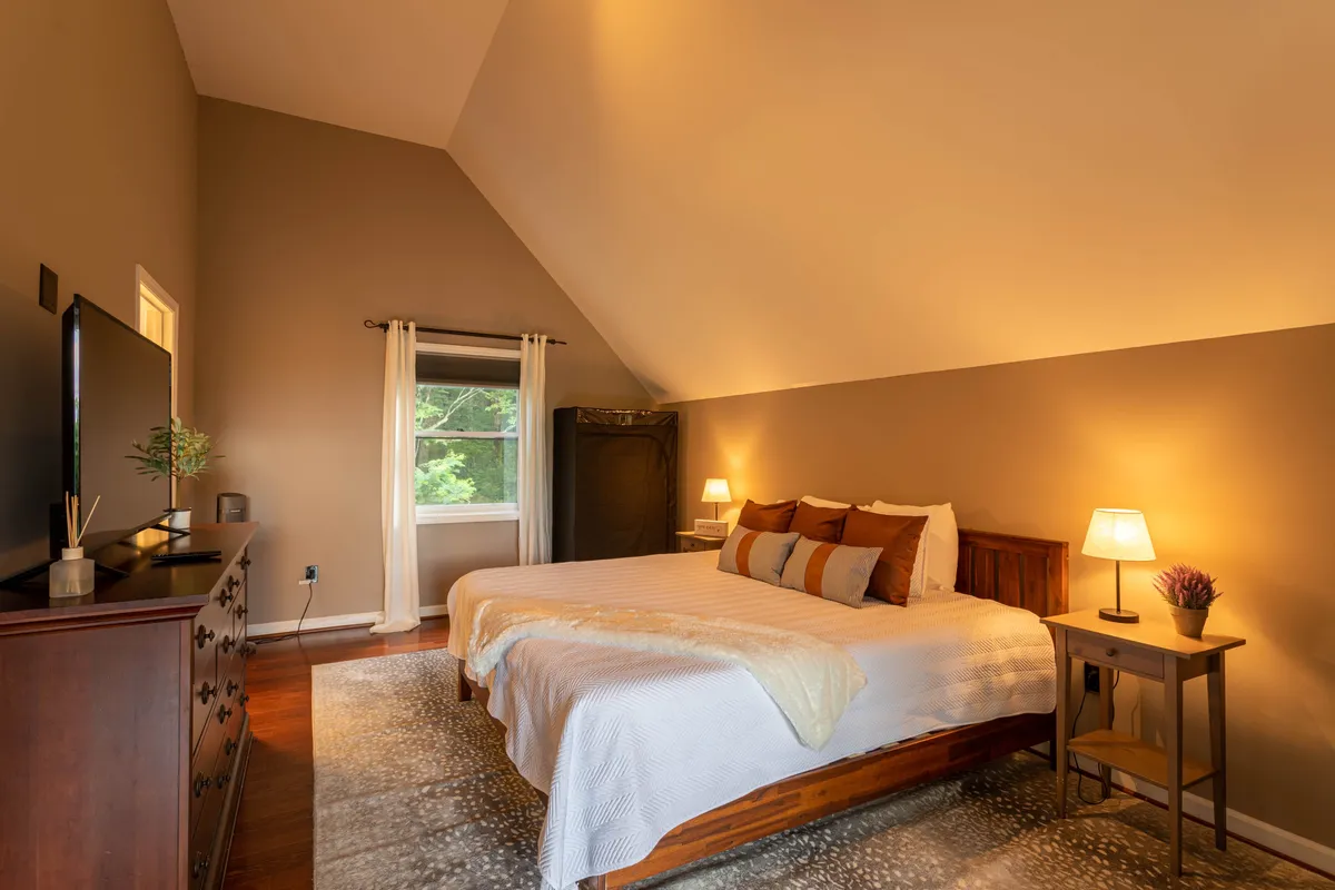 A spacious bedroom with a king-sized bed, wooden dresser, large window inviting in sunlight, and nightstands with lamps. The room feels cozy and perfect for winding down after an adventure-filled day.