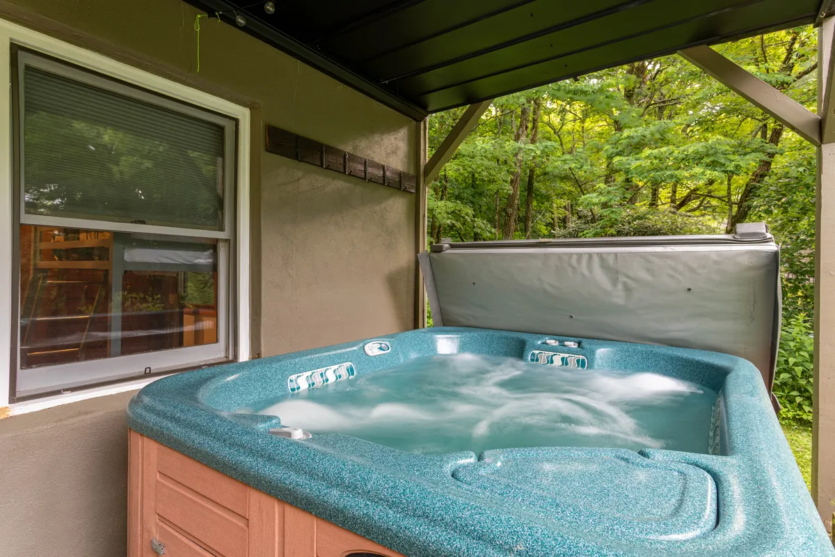 This image shows an inviting outdoor hot tub nestled amid lush greenery, with a window reflecting the tranquil surroundings. The setting is serene, offering both privacy and a deep connection to nature—ideal for group relaxation after a day of adventure.