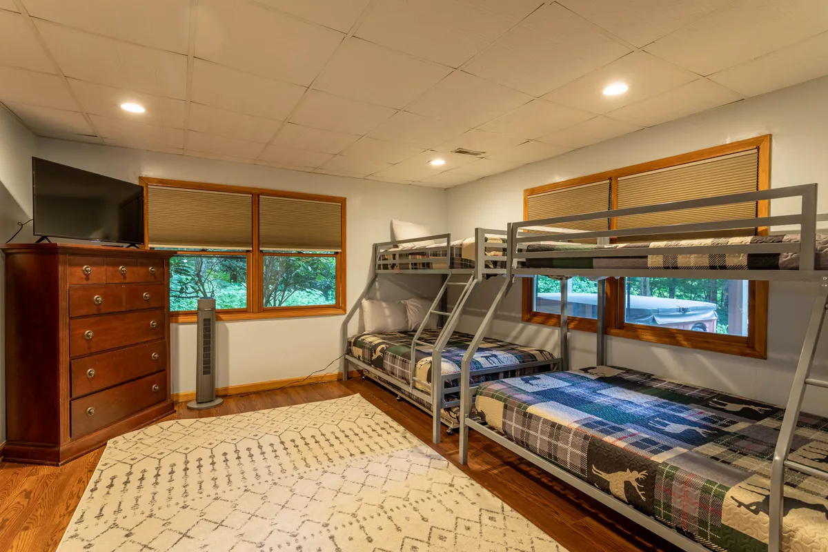 A family-friendly bunk room with twin-over-full bunk beds, a dresser, television, and windows letting in natural light. The playful yet practical space is ideal for kids or groups, offering both entertainment and restful sleep.