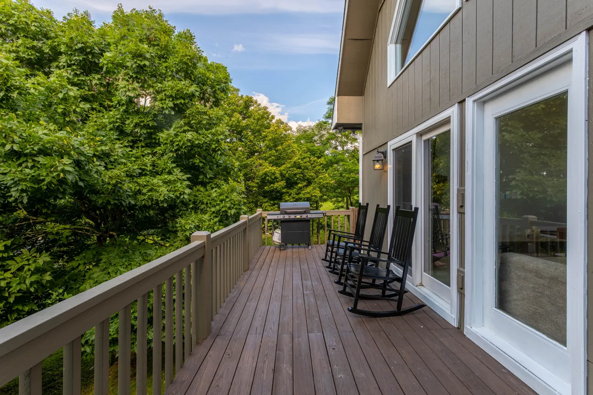An exterior porch with classic rocking chairs, a grill for outdoor cooking, and lush greenery all around. The scene suggests leisurely moments spent soaking in the fresh air and mountain vistas, with the option for sunset views or social gatherings.