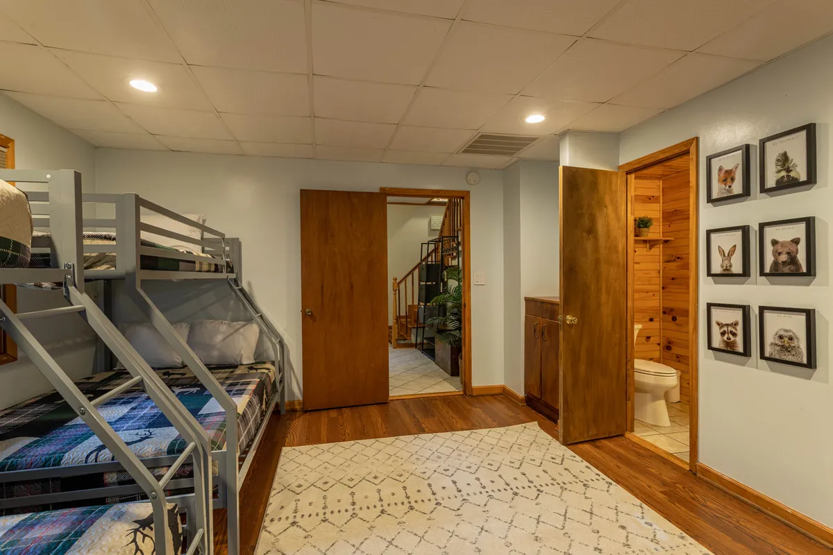 A cozy bunk room with wooden bunk beds, animal-themed wall art, soft rugs, and warm lighting. Positioned near the game room, it offers an easy transition from playtime to rest for younger guests.