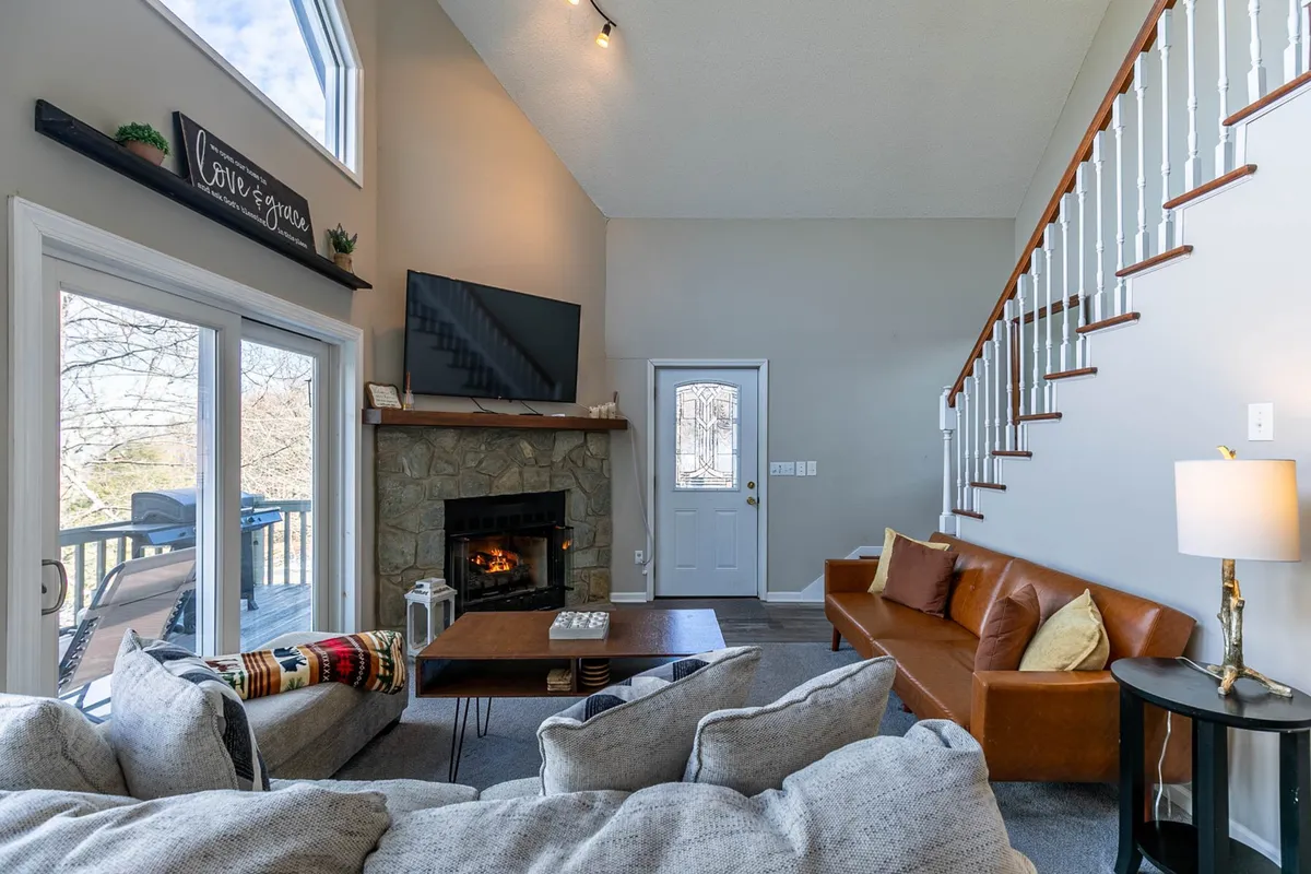 A cozy family room featuring a fireplace, a plush sofa, and windows that offer glimpses of the outdoors. The setting invites relaxation, making it a comfortable gathering spot to warm up together—pets included—after an outdoor excursion.